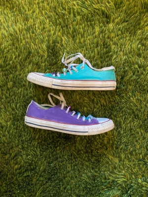 Turquoise/Lila Converse låga sneakers - Unika Converse sneakers i lågt snitt med canvasmaterial. Ena sidan är turkos och andra sidan lila, med vita tår och sulor. Skorna har vita snören dekorerade med färgglada pärlor.