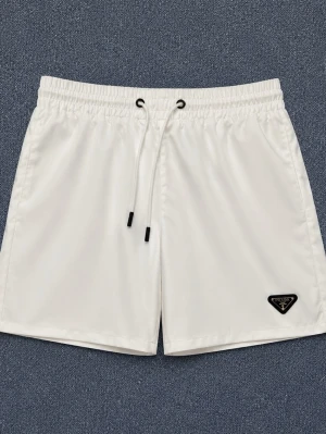 Prada Badshorts - Säljer ett par stilrena vita shorts från Prada med elastisk midja och snörning framtill. Shortsen har en klassisk passform och den ikoniska Prada-loggan på vänster ben. Perfekta för sommaren och tillverkade i ett glansigt syntetmaterial. Följ vår insta @Marknadsveriges. Finns i M och L
