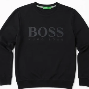 Svart sweatshirt från Hugo Boss - Stilren svart sweatshirt från Hugo Boss med stor BOSS-logga framtill. Tröjan har rund halsringning, ribbade muddar vid ärmslut och nederkant samt en klassisk passform. Perfekt för en clean och modern look.
