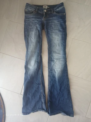 Blå bootcut jeans med slitningar - Snygga blå bootcut jeans med slitningar och ljusare partier framtill. Klassisk femficksmodell med låg midja och dragkedja. Jeansen har kontrastsömmar och är tillverkade i denim. Perfekta för en avslappnad och trendig look.