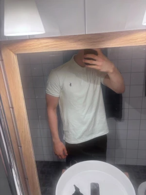 Vit pikétröja från Polo Ralph Lauren L - Klassisk vit pikétröja från Polo Ralph Lauren med korta ärmar och den ikoniska broderade loggan på bröstet. Tröjan har krage och knäppning med två knappar framtill.