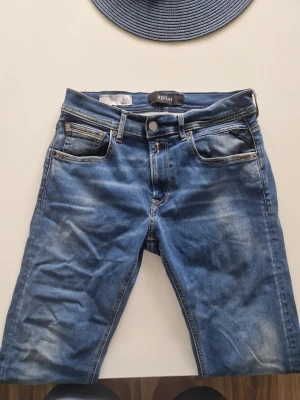Blå Replay Grover jeans, storlek 29 - Säljer ett par snygga blå jeans från Replay, modell Grover. Jeansen har klassisk femficksdesign, normal midja och raka ben. Materialet är slitstarkt denim med snygga slitningar och tvättade detaljer för en cool look. R et på bakfickan har tyvärr ramlat av men annars bra skick 