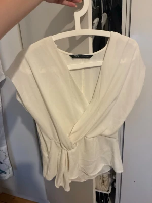 Vit omlottopp från Zara - Säljer en stilren vit omlottopp från Zara med knyt i midjan.