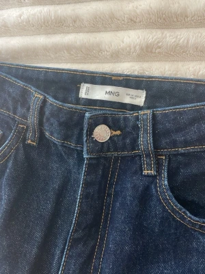 Mörkblå utsvängda jeans från Mango - Säljer ett par mörkblå jeans från MANGO med avklippt stil längst ned. De är i storlek 34 och säljs pga att de blivit för små!