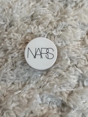 NARS light reflecting Eye Brightener - NARS ”Night Swan” Light Reflecting Eye Brightener i en liten rund burk med vit lock och svart logga. Produkten är en ögonreflektor som ger lyster och ljusreflektion till området runt ögonen. Perfekt för att pigga upp blicken och skapa en fräsch look.