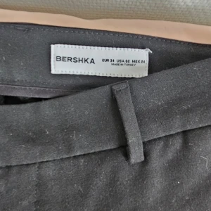 Svarta kostymbyxor från Bershka - Snygga svarta kostymbyxor från Bershka med låg midja, raka ben - klassisk passform. Byxorna har hällor för skärp, diskreta sidofickor och stängs med dragkedja och hake. Perfekta för en clean och stilren outfit!