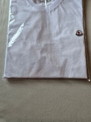 Vit Moncler t-shirt med logga - Snygg vit t-shirt från Moncler med klassisk rund halsringning och liten broderad logga på bröstet. Tillverkad i mjuk bomull som känns skön mot huden. Perfekt för en clean och stilren look.