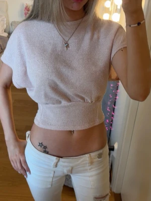 Ljusrosa croppad topp - Säljer en ljusrosa croppad topp med korta ärmar och rund hals. Toppen har en ribbad midja som ger en snygg passform och är i ett mjukt stickat material.