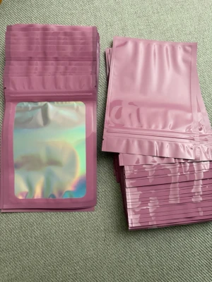 100st Rosa zip-påsar med holografiskt fönster, 15x10 - Säljer 100 stycken  rosa zip-påsar i plast med ett snyggt holografiskt fönster på framsidan. Perfekta för förvaring av småprylar, smycken eller godis. Påsarna är återförslutningsbara och har en modern look med sin glansiga finish. Storlek: 15x10