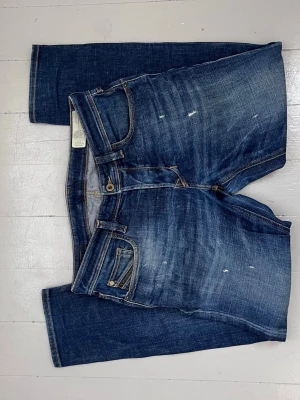 Mörkblå jeans med slitningar - Säljer ett par mörkblå jeans med snygga slitningar och tvättade detaljer. Jeansen har raka ben, klassiska fem fickor och coola bakfickor med V-formad söm. Perfekta för en avslappnad och trendig look.