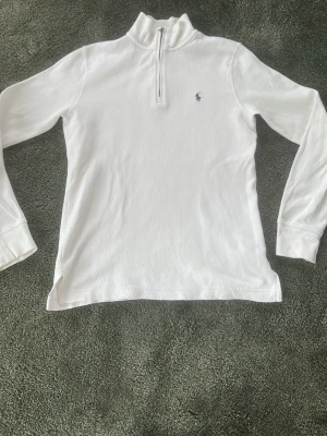 Vit långärmad tröja Polo Ralph Lauren - Klassisk vit långärmad tröja från Polo Ralph Lauren med halv dragkedja och liten broderad logga på bröstet. Tröjan har hög krage och är tillverkad i mjukt bomullsmaterial. Perfekt för en clean och stilren look.
