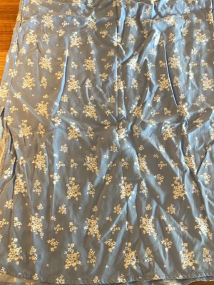 Blå långkjol med blommigt mönster - Snygg blå långkjol med vitt blommigt mönster. Kjolen har en rak passform och är tillverkad i ett lätt, mjukt material som ger ett fint fall. Perfekt för dig som gillar en romantisk och avslappnad stil.
