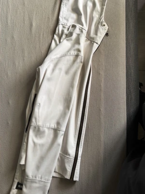 Vit vindjacka från Moncler - Snygg vit vindjacka från Moncler med dragkedja och diskret Moncler-logga på ärmen. Jackan har en minimalistisk design, praktiska fickor och är tillverkad i ett lätt, vindtätt material som passar perfekt för blåsiga dagar.