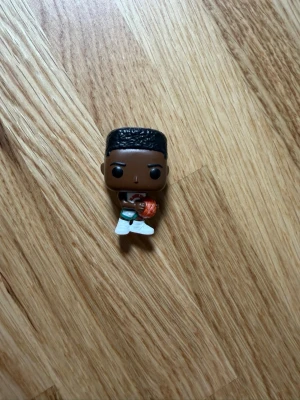 Funko Pop! Lucas from stranger things - Cool Funko Pop! figur i vinyl som föreställer en basketspelare med svart hår, vit tröja, vita shorts och vita skor. Figuren håller en orange basketboll och har typisk Funko Pop-stil med stort huvud och små detaljer.