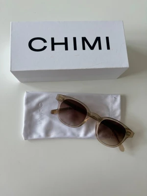 Beige solglasögon från CHIMI - Snygga solglasögon från CHIMI med transparent beige båge och bruna tonade glas. Klassisk, något fyrkantig form som passar till de flesta outfits. Kommer med originalfodral och box. Perfekta för soliga dagar och ger en cool vibe.