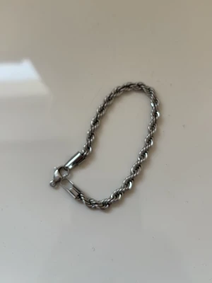 Tjockt silverfärgat kedjearmband - Snyggt armband i silverfärgad metall med tvinnad kedjedesign. Armbandet har en robust karbinhake som lås och passar perfekt för dig som gillar stilrena accessoarer med lite edge. Metallens blanka finish ger ett modernt intryck och armbandet är lätt att matcha med andra smycken. Men har dock en missande bit du kan se de på bilderna.