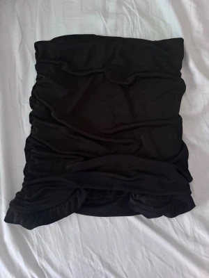 Svart tight kortkjol med rynkade sidor - Säljer en svart tight kortkjol med rynkade sidor. Kjolen har en enkel och stilren design som passar till många olika outfits. Materialet känns mjukt och stretchigt vilket gör den bekväm att bära.