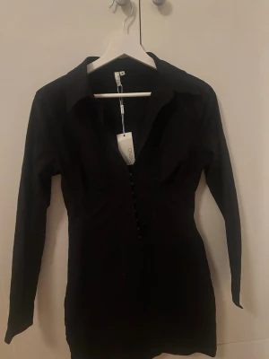 Svart långärmad skjortklänning Nelly - Aldrig använd, prislapp finns kvar. Knäppen vid brösten 