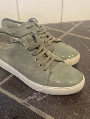 Lanvins - Snygga sneakers i grågrönt mockaliknande material med glansig plastig tå och vita sulor. Skorna har matchande grågröna skosnören och metallfärgade öljetter. Perfekta för dig som gillar en stilren men unik look.