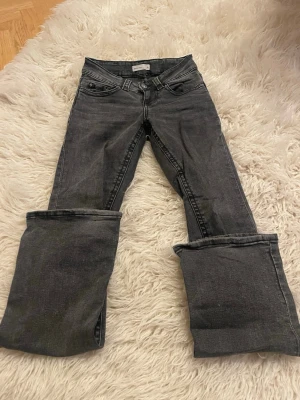 Grå/svart bootcut jeans från Gina - Snygga gråsvarta bootcut jeans från Gina med klassisk femficksdesign och markerade sömmar. Jeansen har en cool tvättad look och vida ben, använda väldigt få gånger och har inga slitningar. 
