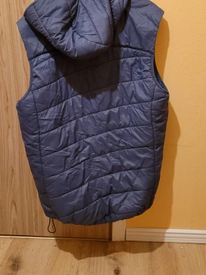 Mörkblå dunväst med huva - Snygg mörkblå dunväst från Xtra med huva och dragkedja framtill. Västen har quiltad design och dragsko nertill för extra passform. Perfekt för lager-på-lager och håller dig varm under kyliga dagar.