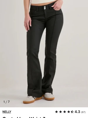 Svarta bootcut jeans från Nelly - Snygga svarta bootcut jeans från Nelly med hög midja och dubbla knappar framtill. Jeansen har klassiska fem fickor och markerade sömmar längs benen. Tillverkade i ett stretchigt material för skön passform och trendig look.