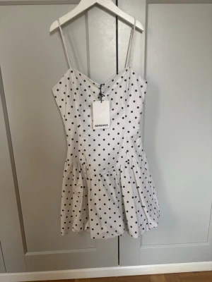 Helt ny vit prickig kort klänning Bershka🫶🏼 - Söt vit kort klänning från Bershka med svarta prickar och tunna axelband. Klänningen har en lätt utställd kjol och smickrande passform, perfekt för varma dagar. Materialet känns mjukt och luftigt.