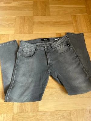 Grå jeans från Replay - Snygga grå jeans från Replay med klassisk femficksdesign och raka ben. Jeansen har diskreta slitningar och logga på myntfickan samt bakfickorna. Riktigt snygg färg nu inför våren. Jeansen är slim fit/replay anbass