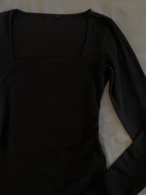 Svart långärmad topp med fyrkantig ringning - En stilren svart långärmad topp med fyrkantig ringning. Toppen har en figurnära passform. Storlek S passar både S och XS.