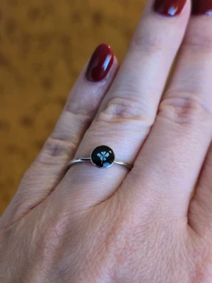 Silverring med blomma - En tunn silverring med en blå blomma ii mitten. Ringen har en minimalistisk design och passar perfekt för dig som gillar stilrena accessoarer med en touch av natur. Rostfritt stål.