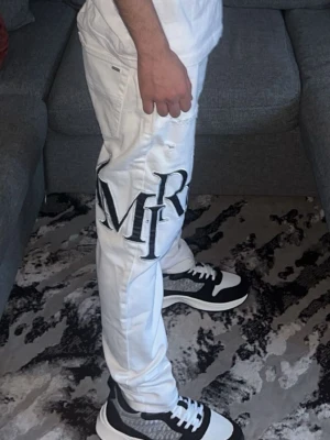 Vita jeans med stora bokstäver - Snygga vita jeans med stora svarta bokstäver tryckta på ena benet. Jeansen har en slim fit-modell och diskreta slitningar för en trendig look. Perfekta för dig som vill sticka ut med din stil.