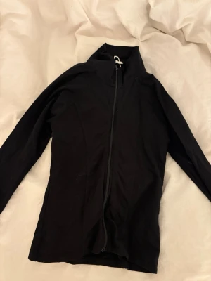 Svart ziptröja med hög krage - Snygg svart ziptröja med hög krage och hel dragkedja framtill. Tröjan har lång ärm och en smal, kroppsnära passform. Perfekt att slänga på sig över en t-shirt eller under en jacka för extra lager.