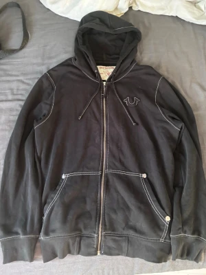 Svart True Religion hoodie med tryck - Säljer en svart zipup från True Religion, köpt på NK för ett tag sen för 1800kr men använder den inte längre.