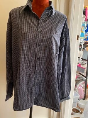 Rutig skjorta med knappar XL - Rutig långärmad skjorta med knäppning framtill och vid ärmslut. Skjortan har en bröstficka på vänster sida. Kragen är klassisk. litet hål, se bild 2! Har alla knappar! 65% polyester 35% Bomull  Inga bilder när den sitter på mig! Katter finns i hemmet!