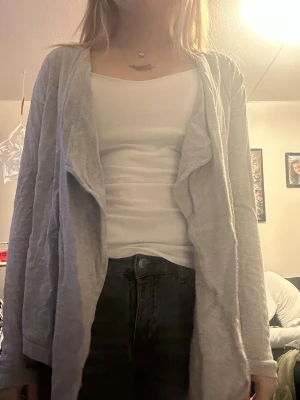 Ljusgrå kofta med vattenfallsärm - Säljer en ljusgrå kofta med vattenfallsärm och öppen framsida. Koftan är tillverkad i ett mjukt och tunt material, perfekt att slänga över en topp. Passar till jeans eller kjol för en avslappnad look. Storlek 158/164