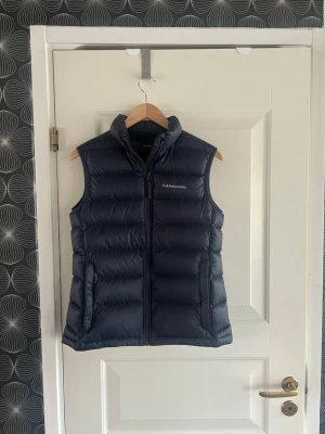 Mörkblå dunväst från Peak Performance - Snygg mörkblå dunväst från Peak Performance med hög krage och dragkedja framtill. Perfekt att slänga över en hoodie eller tröja när det är kyligt ute. Skick 9/10. Använd max 10 gånger. Skriv gärna om ni har frågor