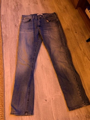 Blå raka jeans från Calvin Klein - Säljer ett par klassiska blå jeans från Calvin Klein med raka ben och femficksmodell. Jeansen har en snygg tvättad look och subtila slitningar. Perfekta för en avslappnad stil och har CK-logga på bakfickan.