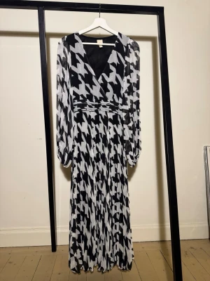 H&M maxiklänning storlek 34 XS plisserad svart/vit - Elegant H&M plisserad maxiklänning med svartvitt hundtandsmönster, djup V-ringning och långa flowy ballongärmar. Klänningen har superfint fall och sitter smickrande i midjan. Dold dragkedja i midjan och helfodrad. Normal storlek 34 (XS). Sparsamt använd och i fint skick.
