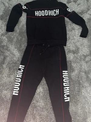 Svarta mjukisbyxor från Hoodrich XS - Säljer ett par svarta mjukisbyxor från Hoodrich i storlek XS. Byxorna har vita logotexter längs benen och tunna röda linjer på sidorna. Dragsko i midjan för skön passform och mjukt material som känns riktigt chill.