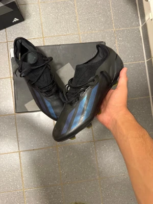 Adidas Crazyfast X ”Nightstrike” FG - Snygga fotbollsskor från Adidas i svart med blå metallic-ränder på sidorna. Skorna har en strumpliknande passform, snörning och greppvänlig sula för spel på gräs. Tillverkade i syntetmaterial för lätt känsla och bra bollkontroll. KVITTO FINNS OCH ORIGINAL BOX TILLKOMMER 🤝