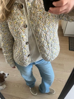 Blommig quiltad jacka med stora knappar - Intressekoll på denna supergulliga quiltade jackan med blommigt mönster i gult, grönt och vitt💞 Jackan har stora bruna knappar framtill och rundad krage. Jackan är boxig och kortare i passformen, perfekt för lager på lager nu till våren🌸 Modellen Viola ifrån Lolly’s laundry