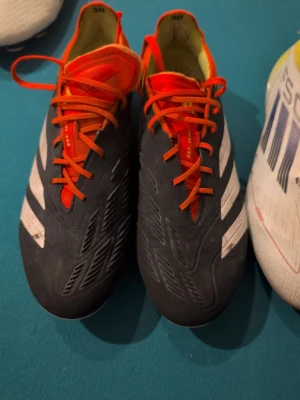 Adidas Predator Elite fotbollsskor - Säljer ett par Adidas Predator Elite fotbollsskor i svart med vita detaljer och orange snörning. Storlek 41 1/3del Bra skick , fina dobbar