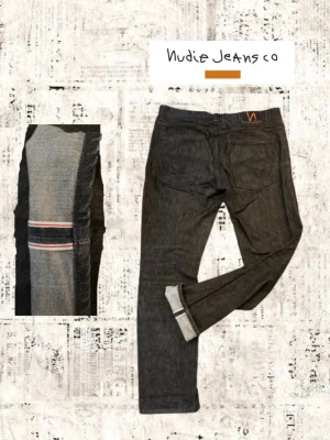 Svarta selvedge jeans från Nudie Jeans - Riktigt snygga svarta selvedge jeans från Nudie Jeans med klassisk rak passform. Jeansen har tydliga selvedge-detaljer i sidsömmen och Nudie-logga på bakfickan. Tillverkade i rå denim för en stilren look. Modellen är Grim Tim! Hör av er vid frågor