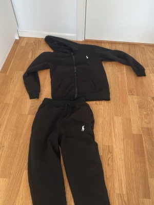 Svarta mjukisbyxor från Ralph Lauren - Säljer ett par svarta mjukisbyxor från Ralph Lauren med dragsko i midjan och den klassiska vita loggan broderad på benet. Sköna och stilrena byxor i mjukt material, perfekta för chill dagar eller när du vill vara bekväm.