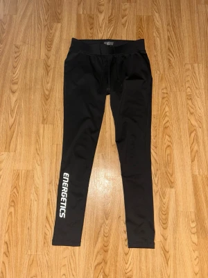 Svarta leggings från Energetics - Snygga svarta leggings från Energetics med vit logga längs ena benet. De har en hög midja och är tillverkade i ett stretchigt material som passar perfekt för träning eller chill. Tight passform och långa ben ger en sportig look. Storlek S - 36/38. Inte använda