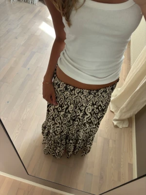 Svartvit långkjol med volang - Säljer en svartvit långkjol med ett unikt mönster och volang nertill. Kjolen har resår i midjan för skön passform och är perfekt för dig som gillar boho-vibbar. Materialet känns lätt och flowy, perfekt för varma dagar.