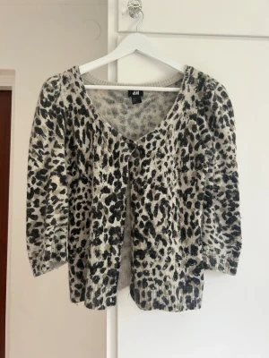 Leopardmönstrad kofta från H&M - Snygg kofta från H&M med leopardmönster i svart och beige. Koftan har trekvartsärmar, rund halsringning och knäppning framtill.