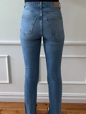 Gina Tricot Perfect Jeans – Straight, High Waist TALL, mörkblå med slits, Storlek 36 (Långa) - Mycket bra skick. Använda ett fåtal gånger. Mörkblå Perfect Jeans med high waist och straight fit. Slits och fransad fåll, något tajtare modell.  Långa ben – passar ca 175–180 cm. Normal i storlek, inga defekter.  Säljer fler modeller i samma storlek, se profil.