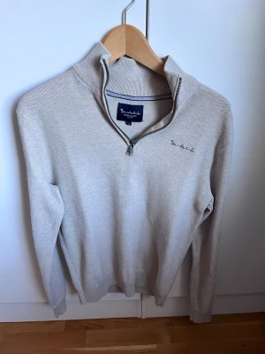 Beige stickad tröja med halvzip - Snygg beige stickad tröja från Bondelid med halvzip och hög krage. Tröjan har diskret broderad logga på bröstet och ribbade muddar vid ärmslut och nederkant. Perfekt för lager på lager och enkel att matcha.