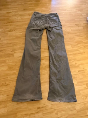 Gröna jeans  - Säljer ett par gröna bootcut jeans med klassiska fem fickor och vita sömmar på bakfickorna. Jeansen har låg midja och vida ben, perfekta för en avslappnad och trendig stil. Materialet känns mjukt och följsamt, troligen bomullsblandning. Finns slitningar och lite missfärgning längst ner på byxan, se sida bilden!!